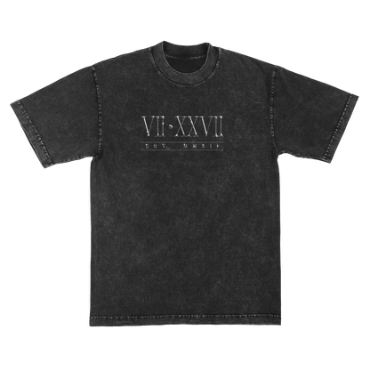 A washed black short-sleeve t-shirt with a white graphic print on the chest featuring Roman numerals 'VII•XXVII' and the text 'EST. MMXII'.